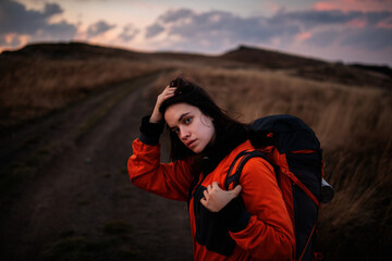 Portrait of a young tourist woman with a backpack straightening her long hair. Young beautiful woman traveling in the mountains - 363322988