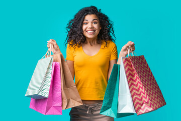 Portrait of happy beautiful dark skinned girl holding piles of shopping bags on both hands isolated...