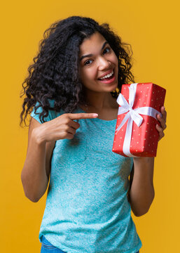 Vertical shot of happy smiling african american girl poiting with index finget at the gift  box in her hand