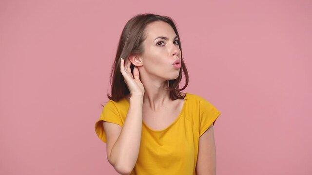 Beautiful brunette young woman girl 20s years old in yellow t-shirt posing isolated on pastel pink background studio. People lifestyle concept. Looking camera try to hear you with hand at ear say what