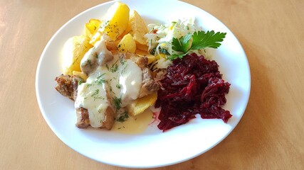 Two fried slices of pork meat with potatoes and beetroot salad on a plate