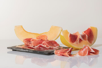 Thin slices of cured ham on a dark plate surrounded by melon slices, one of them with cured ham on top .