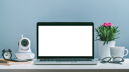 Front view of laptop with white blank screen standing at the office desk with flower pot, web-camera, coffee cup and office supplies