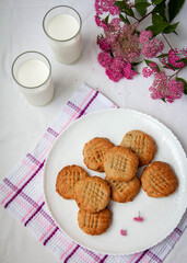 homemade peanut cookies with milk and pink flowers on the white background