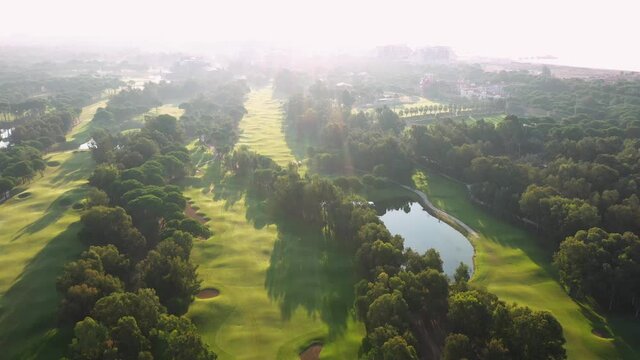 Aerial view of seaside town on a sunny day. Picturesque summer landscape of resort town with green golf field, trees and lake. View from drone.