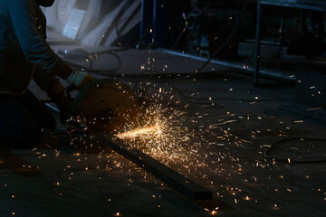 The metal worker cutting a steel material with circular saw machine and sparks in the workshop.
