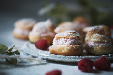 closeup of raspberry creampuffs with fresh raspberries and powdered sugar
