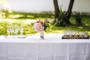 Bouquet of flowers and empty glasses on a table in a garden during a summer day before a toast.