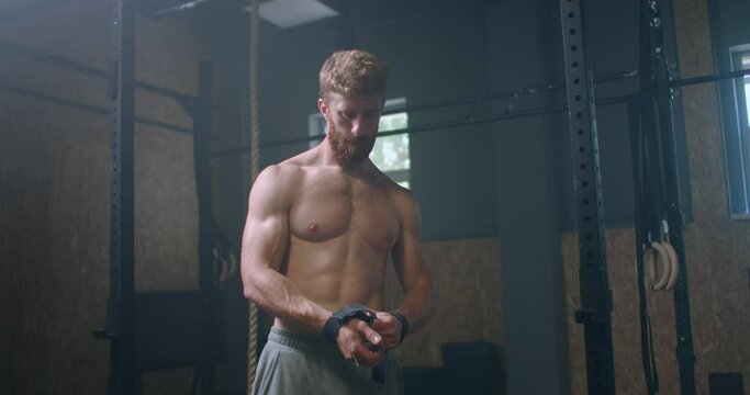 Young athletic Caucasian man changing, putting weight lifting straps on in gym locker room before workout slow motion. ties arms to barbell with fitness straps. 