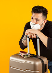 man with suitcase, passport and surgical mask, tired of flight delays by covid-19