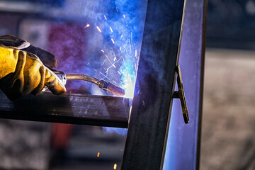 The welder is welding a structural steel with gas metal arc welding ( GMAW ) in the workshop.