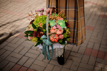 Close-up on wicker basket with flower arrangement in woman's hand.