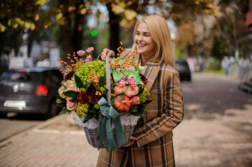 beautiful smiling woman in coat holds basket with flowers inside.
