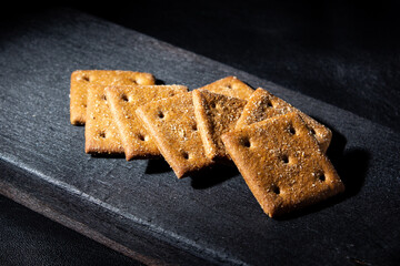 Rye square crackers with salt on a burnt wooden board, on a leather background, low key, brutal style