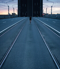 a road with rails stretching away into the horizon and a girl standing in the middle of a beautiful sunrise against the backdrop of a drawbridge