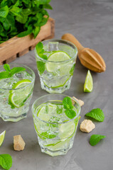 Fresh summer mojito drink with lime slices, mint, ice cubes and brown sugar in a glass on a dark background. Vertical, copy space.