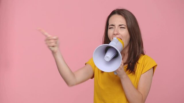 Fun crazy young woman girl 20s years old in yellow t-shirt posing isolated on pastel pink background studio. People lifestyle concept. Point aside scream in megaphone announces discounts sale Hurry up