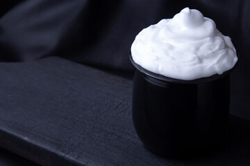 Cream in black plastic cup on burnt wooden board, leather background