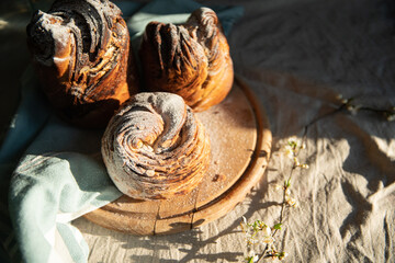 Homemade cruffin breads with dried fruits, cocoa and cinnamon fillings on wooden board and blooming cherry twig on linen tablecloth .