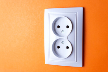 White socket with two plugs on orange wall