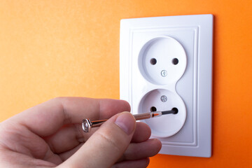 A man inserts a screwdriver into a white outlet, the danger of electricity, electrical damage, work injuries
