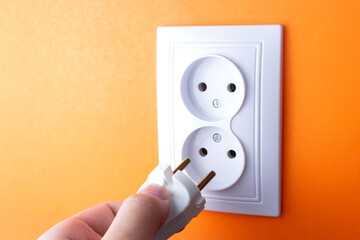 Man inserts plug into white outlet with two plugs on orange wall