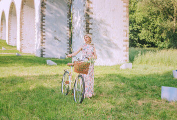 Fototapeta premium Pretty woman with her bicycle on the bridge aqueduct background in summertime season