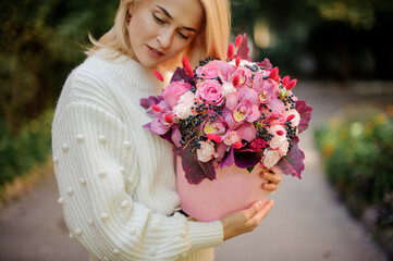 Fototapeta premium beautiful woman neatly holds pink round box with flowers inside