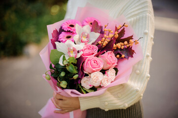 Close-up of bouquet with roses, gerbera, orchids and berries in the hands of woman.