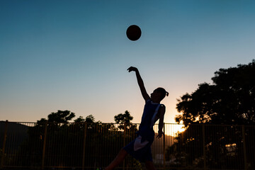 Fototapeta na wymiar Basketball. Silhouette of a teenage boy jumps and throws a ball into up. Sunset sky on the background. Copy space. Concept of sports games