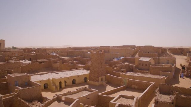 Aerial drone shot rising from rooftop level into the air to reveal the desert town of Chinguetti in Mauritania surrounded by the sahara desert in the background landscape.