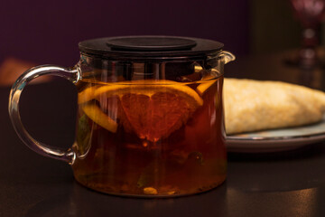 Citrus fruit tea in a transparent teapot against a dark background. Drinks in the cold season.