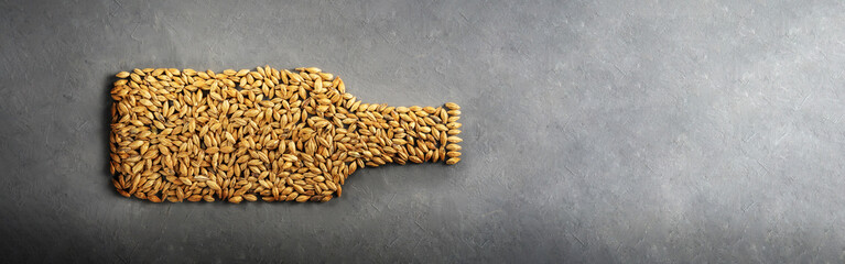 Malt grains are laid out as a beer bottle on a grey concrete background.