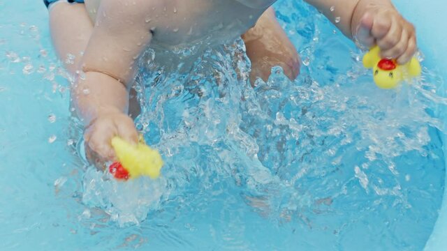 Childs hands with yellow rubber ducks splashes water during swimming in pool outdoors at summer. Little baby boy having fun. Concept of healthy lifestyle, family, leisure in summer. Slow motion.