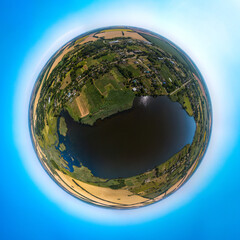 Fototapeta premium Blue pond on the Zelenchuk II river near the village of Peschanoe (Krasnodar Territory, South of Russia) surrounded by wheat fields - aerial drone little planet 360 panorama on a sunny day