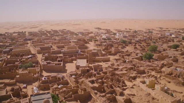 Aerial drone orbit shot of the desert town Chinguetti in Mauritania. Circling the town centre from above showing the entire town surrounded by Sahara desert dunes in the distance.