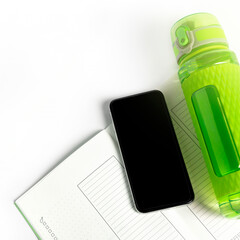 Mobile phone mock up, green training sport bottle and trainingdiary on white background. Workout or fitness concept flat lay with copy space and bright light flare square size