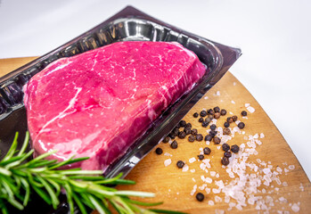 Vacuum-packed beef steak and spices on wooden chopping board