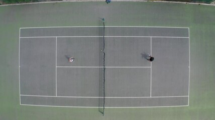 Top down aerial drone shot of a couple playing tennis on an outdoor hard court
