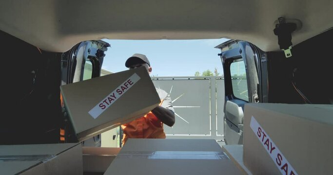 courier with protective mask and gloves delivers parcel labeled with stay safe warning claim at the entrance to the house gate,inside car point of view