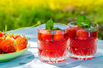 Strawberries in plate on the table and fresh drinks with mint on a sunny day