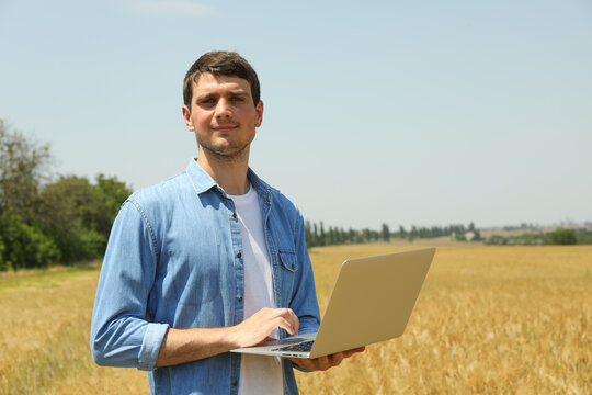 Young man with laptop in barley field. Agriculture business. Farming