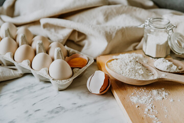 Baking ingredients with eggs, wheat flour, egg yolks for pastry. Cake, pasta or dough recipe ingredients. Top view and flat lay on marble table with copy space
