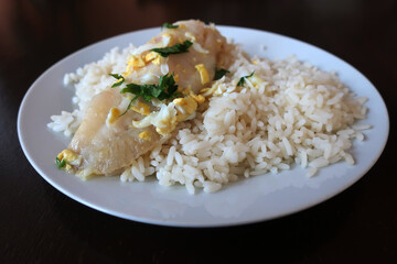 steamed fish with rice, sprinkled with grated egg and herbs on a white plate in the dining room