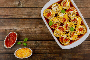 Homemade lasagna rolls in a baking dish on a wooden background. Top view.