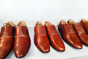Row of Classic brown leather men's shoes on white shelf in a store. Fashion classical polished brown men's shoes on shelf. Sale and shopping concept. Selective focus