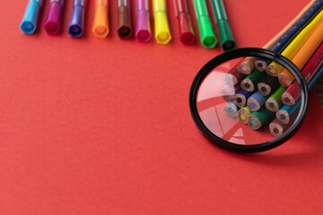 Colored pencils and lupe on bright red background. Back to school flatlay, top view.