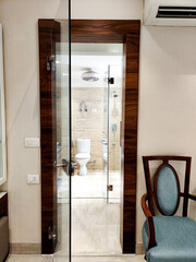 Glass doorway leading to a washroom with the commode visible and blue chair on the side