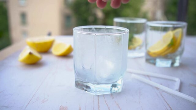 putting ice cubes into the glass for soda water with mint and lemon. refreshing summer cocktail concept with tonic or transparent alcohol