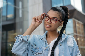 Portrait of beautiful African American woman wearing stylish eyeglasses, standing on the street and...